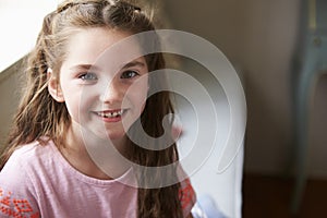 Portrait Of Smiling Young Girl Sitting On Window Seat At Home