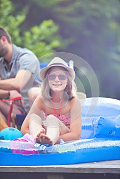 Portrait of smiling young girl wearing a hat and glasses while sitting in pool raft at pier