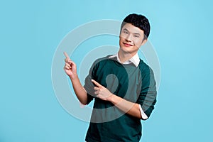 Portrait of smiling young handsome Asian man in green casual shirt pointing to empty copy space isolated on light blue background