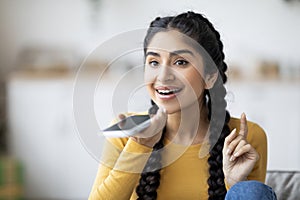 Portrait Of Smiling Young Indian Female Recording Voice Message On Smartphone