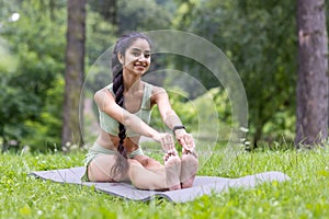 Portrait of a smiling young Indian woman sitting in the park on a rug in shabby clothes, doing sports and yoga, doing