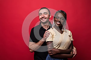 Portrait of a smiling young interracial couple hugging and looking at camera isolated on the red background