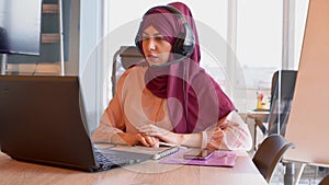 Portrait of smiling young islamic woman in hijab with microphone and working in call center. Arab businesswoman working