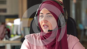 Portrait of smiling young islamic woman in hijab with microphone and working in call center. Arab businesswoman working