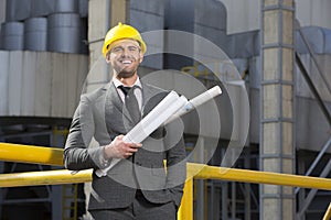 Portrait of smiling young male architect holding blueprints outside building