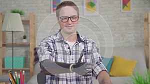 Portrait smiling young man with a bionic prosthetic hand gives a thumbs up sitting at a table