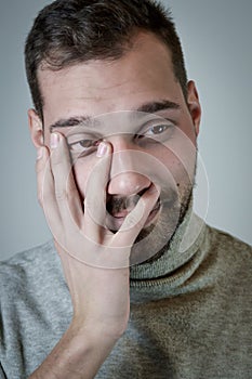 Portrait of a smiling young man covers his face with an ironic and fondling look