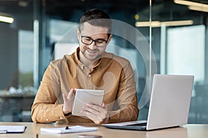 Portrait of a smiling young man designer, engineer, architect sitting in the office behind a notebook and works, draws