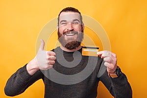 Portrait of smiling young man holding credit card and showing thumb up