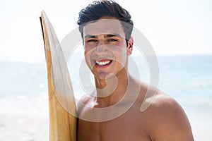 Portrait of smiling young man holding surfboard at beach