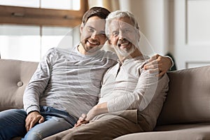 Portrait smiling young man hugging mature father, sitting on couch