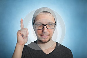 Portrait of smiling young man pointing upwards while standing against blue background. Vertical shot