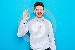 Portrait of smiling young man showing okay gesture isolated on blue background
