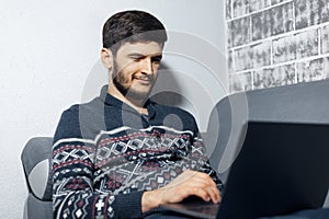 Portrait of smiling young man, sitting on sofa home and using laptop.