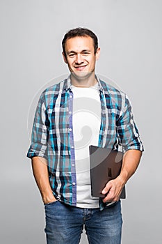 Portrait of a smiling young man standing with laptop against gray background