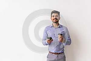 Portrait of a smiling young man using smartphone and holding cup of coffee isolated on a white background
