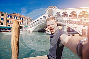 Portrait smiling young man in Venice, Italy taking selfie against backdrop great canal and bridge. Concept travel