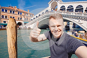 Portrait smiling young man in Venice, Italy taking selfie against backdrop great canal and bridge. Concept travel