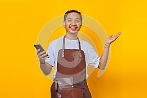 Portrait of smiling young man wearing apron holding mobile phone showing copy space in palm and holding mobile phone