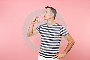 Portrait of smiling young man wearing striped t-shirt holding and drinking clear fresh pure water from glass isolated on