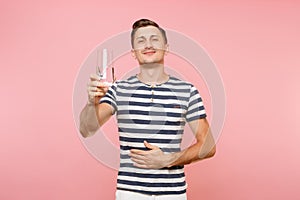 Portrait of smiling young man wearing striped t-shirt holding and drinking clear fresh pure water from glass isolated on