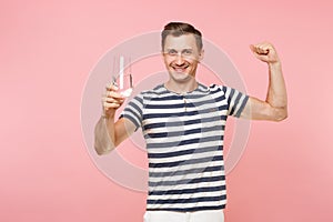 Portrait of smiling young man wearing striped t-shirt holding and drinking clear fresh pure water from glass isolated on