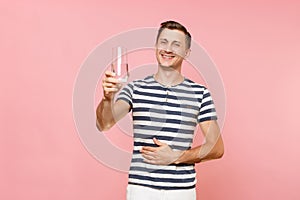 Portrait of smiling young man wearing striped t-shirt holding and drinking clear fresh pure water from glass isolated on