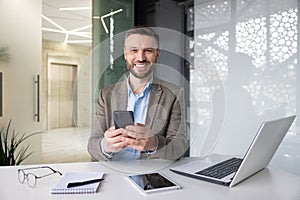 Portrait of a smiling young man working in the office with documents and a notebook, sitting at a desk and using a