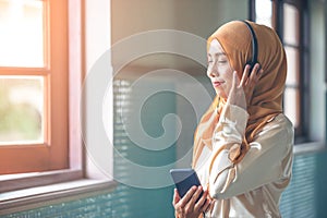 Portrait of a smiling young modern arabian woman closing eyes, holding mobile phone and listening the music to headphone