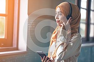 Portrait of a smiling young modern arabian woman holding mobile phone and listening the music to headphone