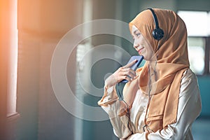 Portrait of a smiling young modern arabian woman holding mobile phone and listening the music to headphone