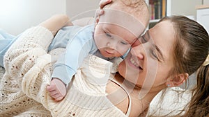 Portrait of smiling young mother hugging and embracing her little baby son while lying on floor. Concept of family