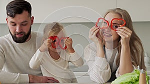 Portrait of a smiling young mother and little daughter holding circles of red pepper as glasses, looking at the camera