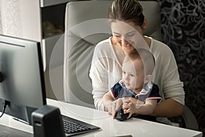 Portrait of smiling young mother showing her baby son how to use computer mouse