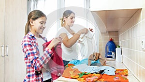 Portrait of smiling young mother with teenage daughter folding clothes after laundry