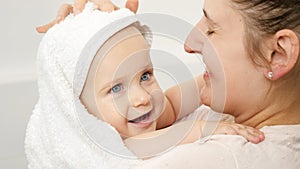 Portrait of smiling young mother wiping wet hair and head of baby son after having bath. Concept of children hygiene