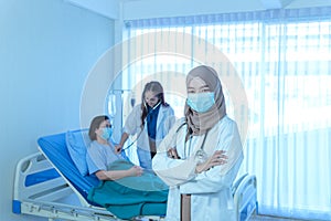 Portrait of smiling young muslim female doctor arms crossed stand in hospital with medical team working on the background