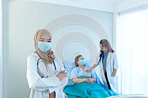 Portrait of smiling young muslim female doctor arms crossed stand in hospital with medical team working on the background