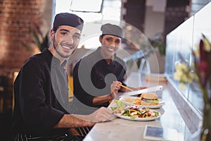Portrait of smiling young wait staff sitting with food and clipboard at counter