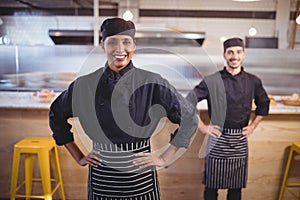 Portrait of smiling young wait staff standing with hands on hip against counter