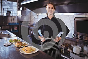 Portrait of smiling young waiter standing with hands on hip by food