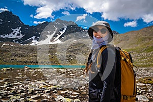 Portrait of a smiling young woman. In the background is a quiet lake and a mountain range. Traveler girl in stylish