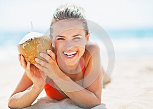 Portrait of smiling young woman on beach holding coconut