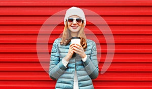 Portrait smiling young woman with cup of coffee wearing a jacket and white hat on red background