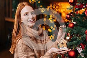 Portrait of smiling young woman decorating Christmas tree beautiful toy at cozy living room.