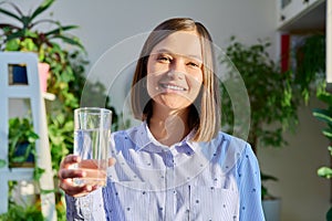 Portrait of smiling young woman with glass of water posing at home