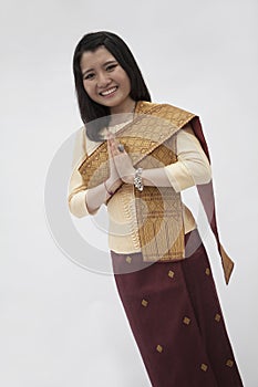 Portrait of smiling young woman with hands clasped together in traditional clothing from Laos, studio shot