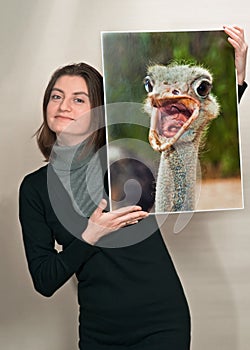 Portrait of a smiling young woman holding a photo of an ostrich with its mouth wide open