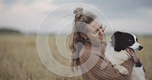 Portrait of smiling young woman kissing doggy in a field. Dog lover stylish girl wearing sunglasses hugging her doggy