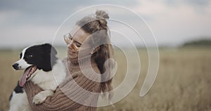 Portrait of smiling young woman kissing doggy in a field. Dog lover stylish girl wearing sunglasses hugging her doggy